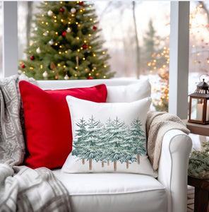 Cozy winter chair sitting by the fireplace. There’s a Christmas tree in the background. A warm throw is over the side of the chair. Our 18 x 18” white pillow features a graphic with snowy pine trees. Simple and beautiful. Pillow insert is included.