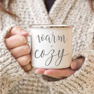 Picture of 11 oz white enamel Camp Coffee Mug with Silver Rim.  Graphic of Warm and Cozy in Grey